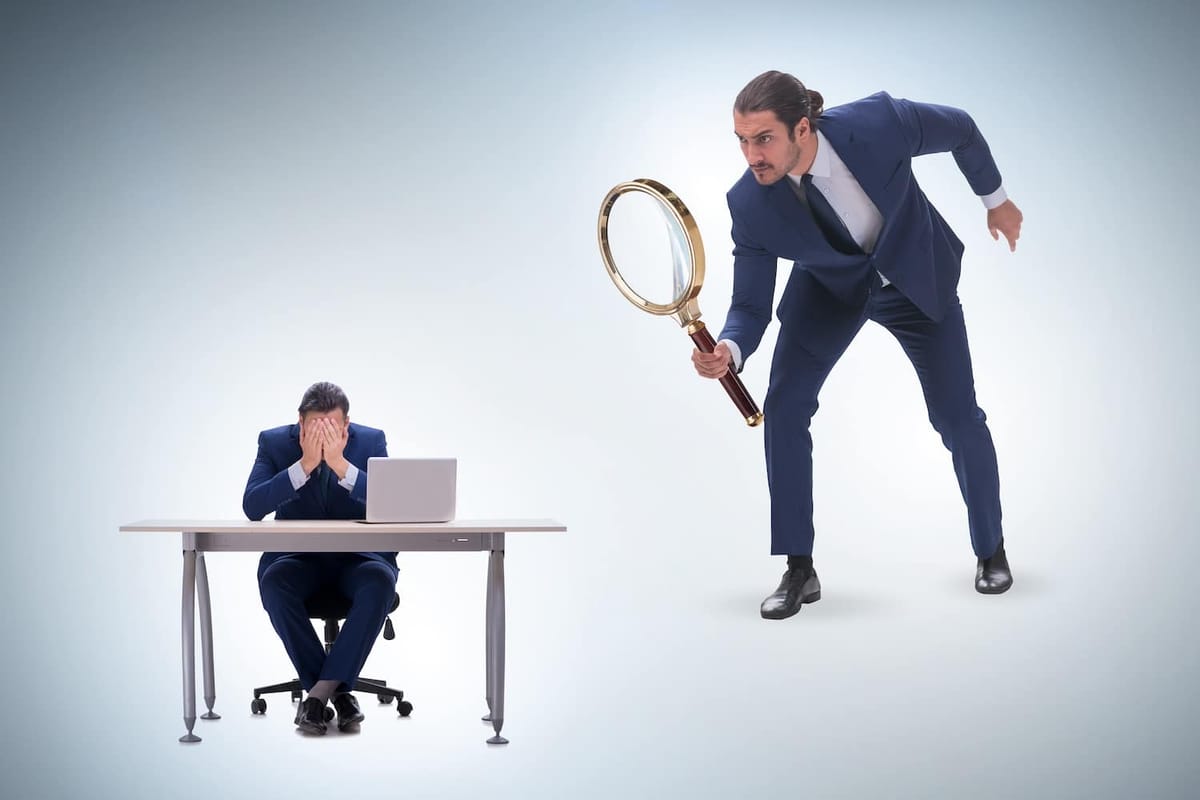 Manager hovering with magnifying glass over employee.
