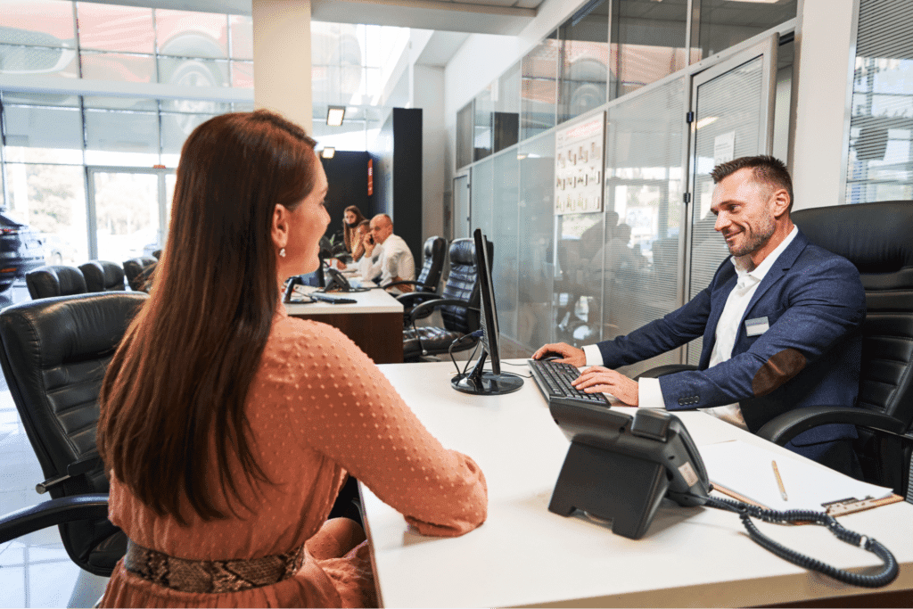 Friendly customer service representative assisting a client at a desk.