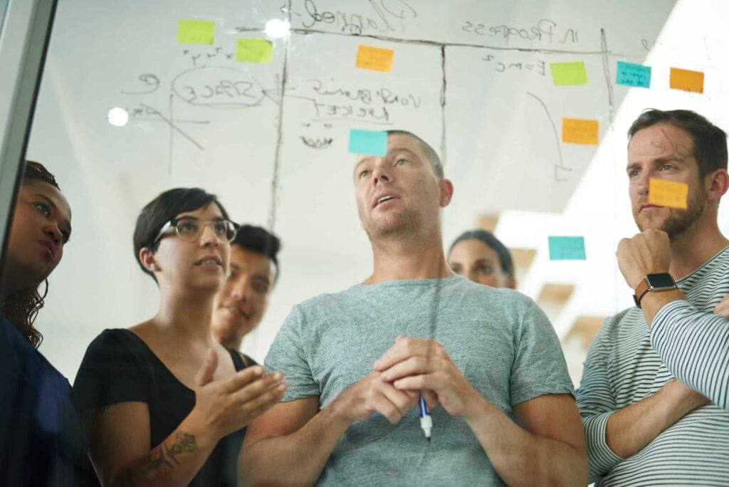 Team brainstorming and planning strategies using sticky notes on a glass board.