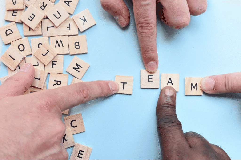 Hands arranging letter tiles to spell TEAM, symbolizing collaboration and high-performing teams.