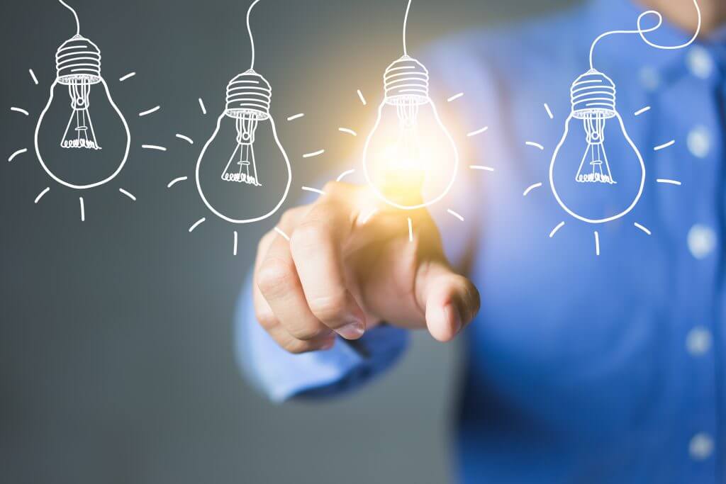 A man in a button down touches a lit light bulb, meant to convey the need for innovation in business during an age of rapid change and evolution in markets across the world.