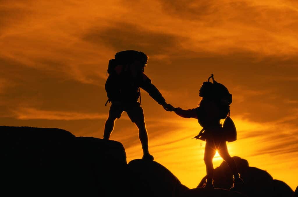 Two team members help each other hike up a mountain. That's a lot of team trust in their workplace.