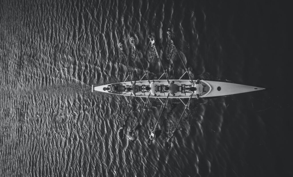 An image of a team working together to move a rowboat represents how using a Kanban System approach can help set team direction
