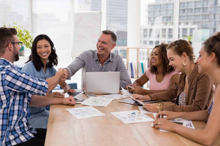 Executives collaborating and celebrating continuous improvement through handshakes in a modern meeting.