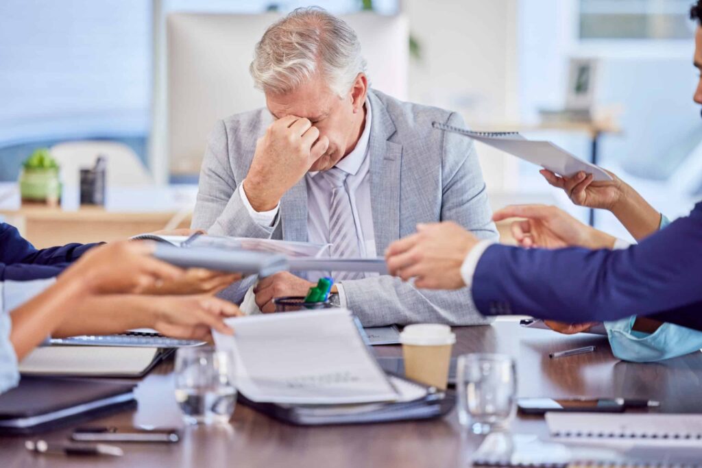 Business owner stressed during a meeting, overwhelmed by transformation efforts and paperwork.