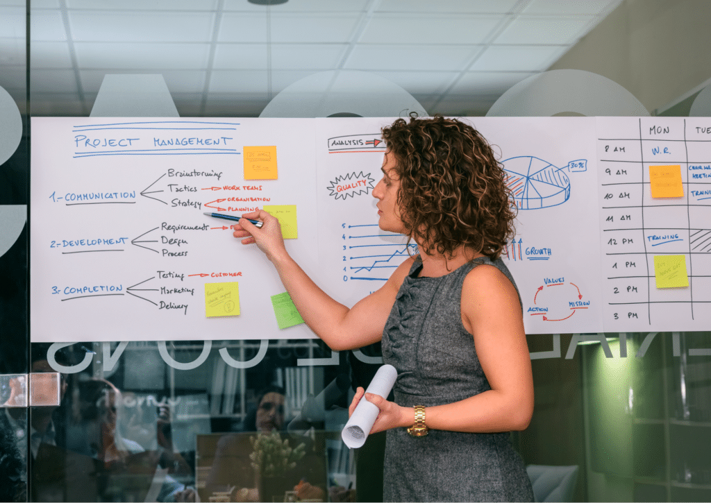 Woman presenting effective project management strategies on a whiteboard.