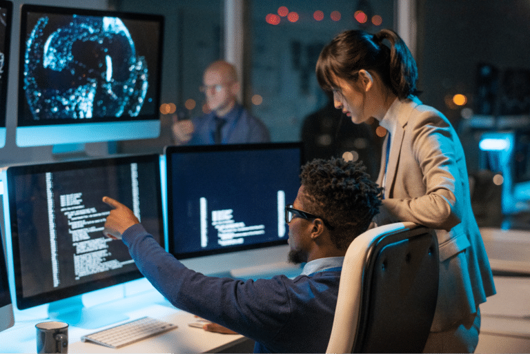Teams collaborating on tech solutions in a modern workspace with multiple screens.