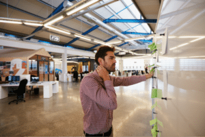 Man brainstorming ideas on a modern workspace whiteboard with sticky notes.