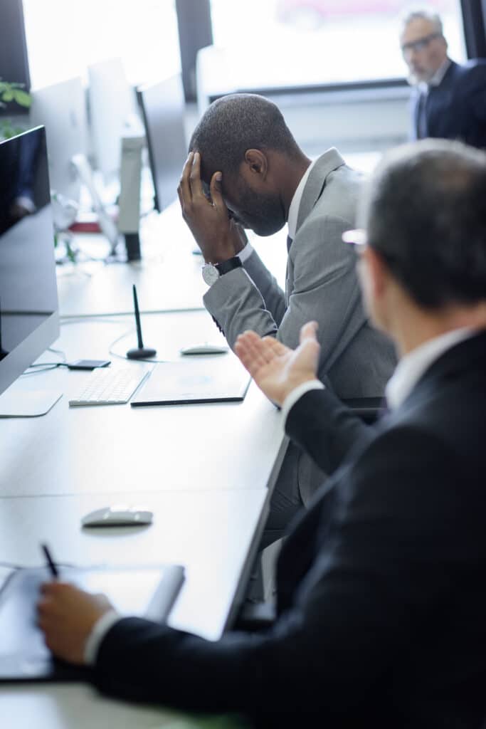 Stressed businessman and colleague arguing at office meeting, highlighting workplace conflict.