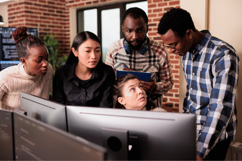 Team members collaborating and brainstorming around a computer screen in an office setting.