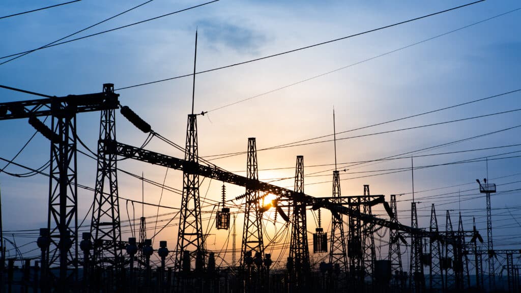 Silhouette of power lines against a sunset sky in an electricity grid.