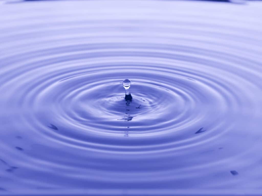 Water drop creating ripples in calm blue water, showcasing fluid motion and tranquility.