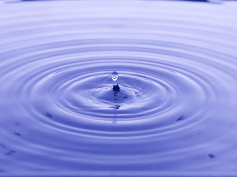 Water drop creating ripples in calm blue water, showcasing fluid motion and tranquility.